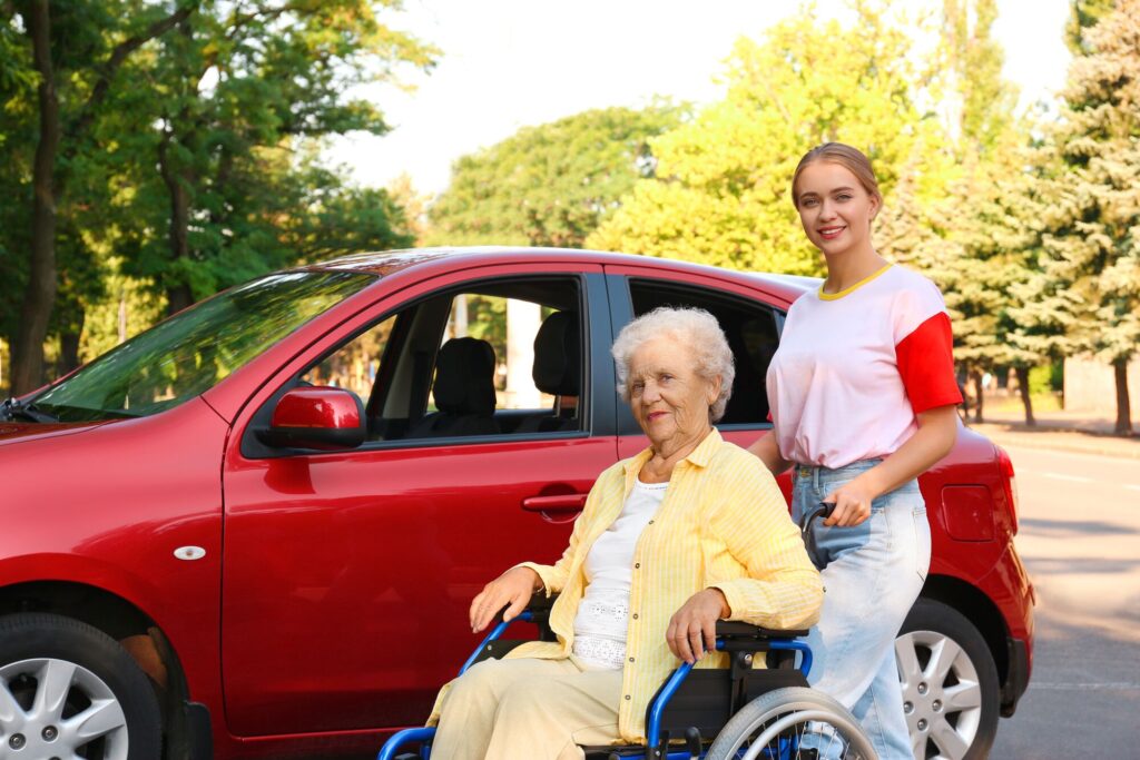 Care giver helping an elderly woman on a wheelchair near the red car